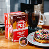 A 12 count box of Donut Shop Coffee Pods sitting on a table next to a sprinkle donut