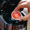 Someone placing an Original Medium Roast Coffee Pod into a brewing machine